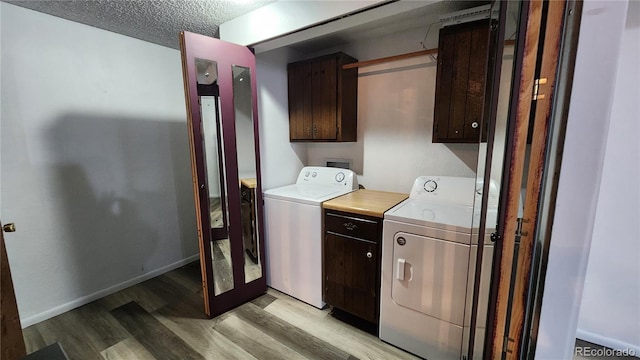 laundry room with washing machine and clothes dryer, cabinets, a textured ceiling, and light wood-type flooring