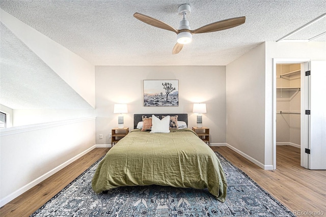 bedroom featuring hardwood / wood-style floors, a spacious closet, a textured ceiling, and ceiling fan