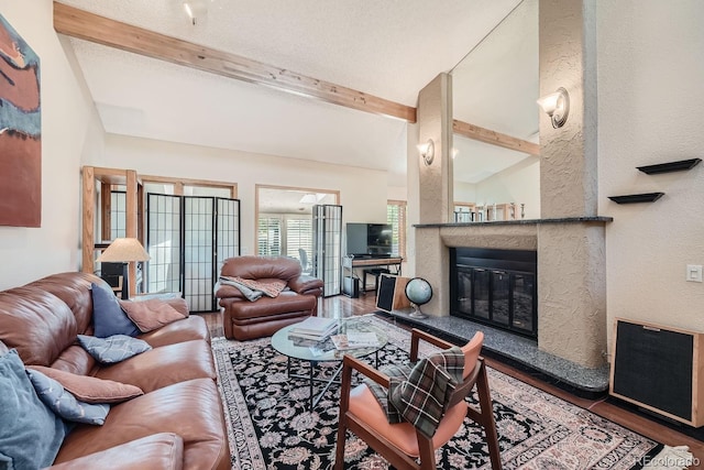 living room featuring lofted ceiling with beams, a textured wall, a fireplace, and wood finished floors