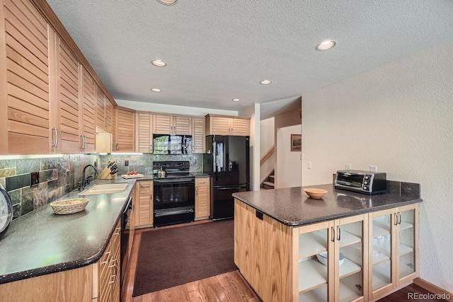 kitchen featuring wood finished floors, dark countertops, a sink, backsplash, and black appliances