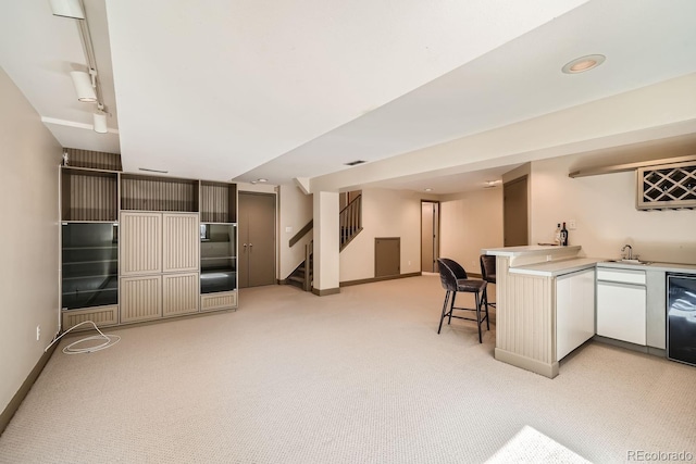 kitchen with a breakfast bar, a sink, light countertops, light carpet, and white cabinetry