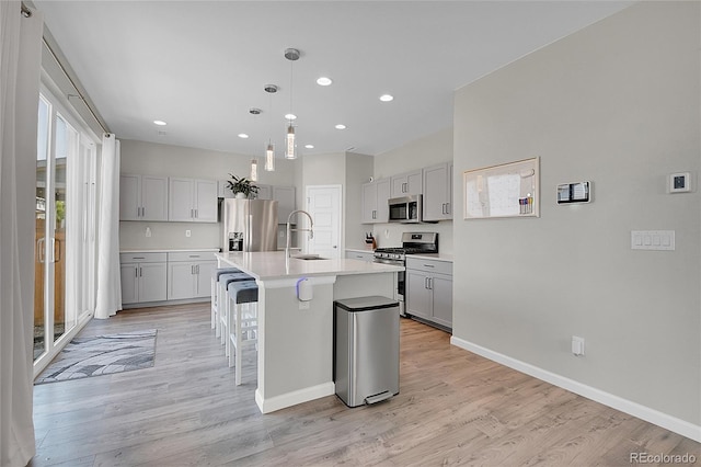 kitchen with pendant lighting, appliances with stainless steel finishes, sink, a kitchen island with sink, and light hardwood / wood-style flooring