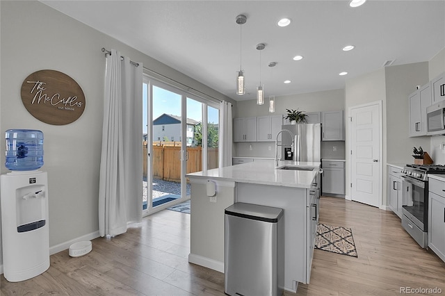 kitchen with sink, light wood-type flooring, a kitchen island with sink, and appliances with stainless steel finishes