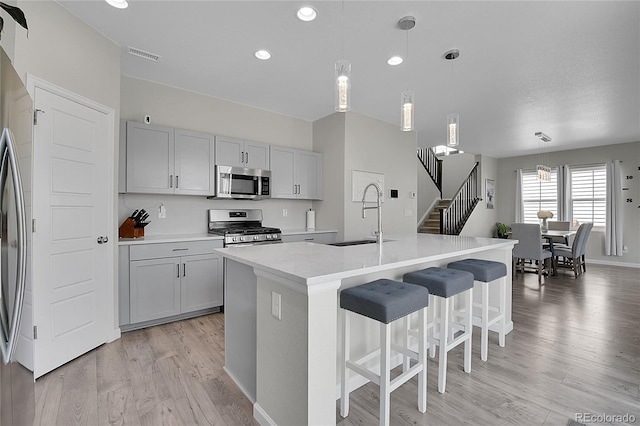 kitchen with pendant lighting, appliances with stainless steel finishes, sink, a kitchen island with sink, and light hardwood / wood-style floors