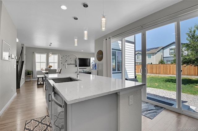 kitchen with an island with sink, plenty of natural light, stainless steel dishwasher, and decorative light fixtures