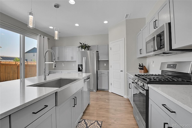 kitchen featuring light hardwood / wood-style flooring, hanging light fixtures, sink, light stone countertops, and stainless steel appliances