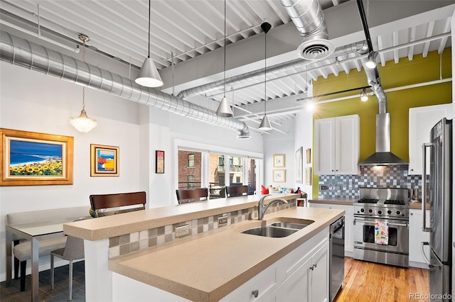 kitchen with appliances with stainless steel finishes, a sink, wall chimney range hood, and light countertops