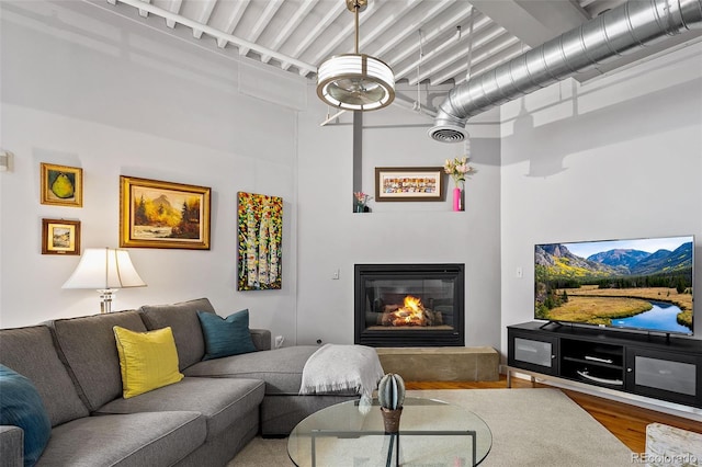 living area featuring a glass covered fireplace, wood finished floors, and a high ceiling