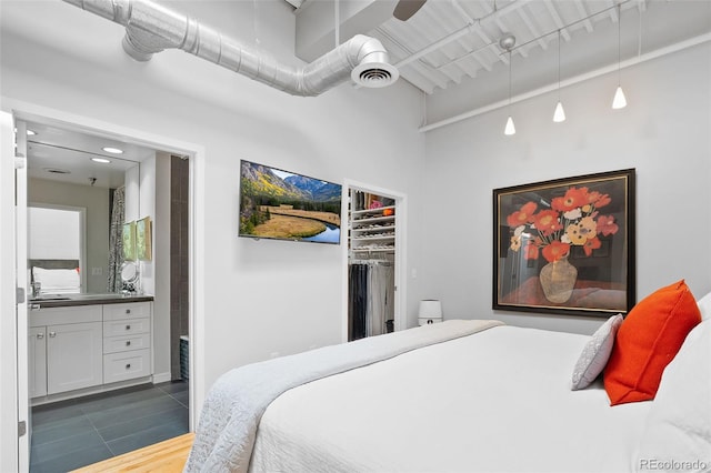 bedroom featuring ensuite bath, a spacious closet, a closet, wood finished floors, and a ceiling fan