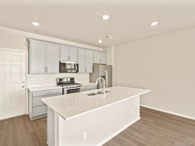 kitchen featuring gray cabinets, appliances with stainless steel finishes, sink, and a center island with sink