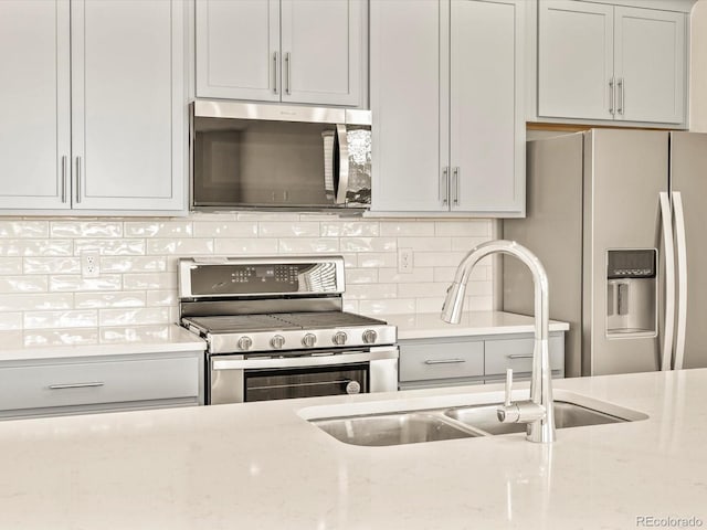 kitchen featuring light stone counters, appliances with stainless steel finishes, sink, and backsplash