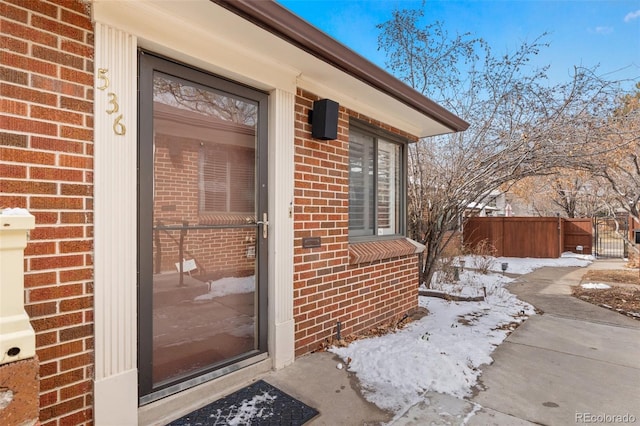 snow covered property entrance featuring fence and brick siding