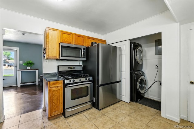 613 S Union Blvd, Colorado Springs, CO 80910 - kitchen featuring appliances with stainless steel finishes, stacked washing machine and dryer, dark countertops, brown cabinets, and light tile patterned flooring