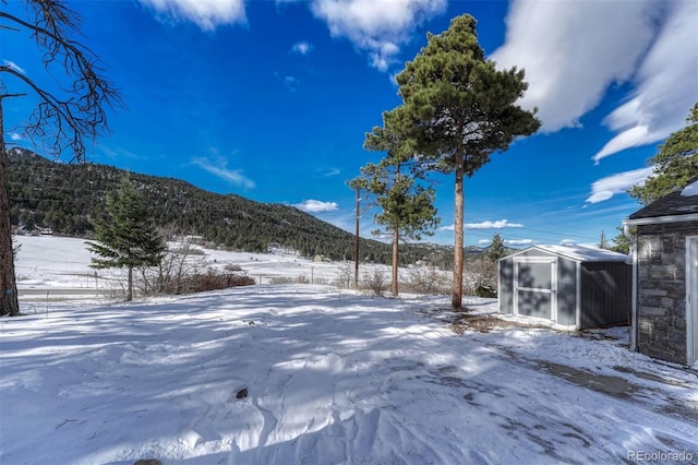 snowy yard with a mountain view and a storage unit