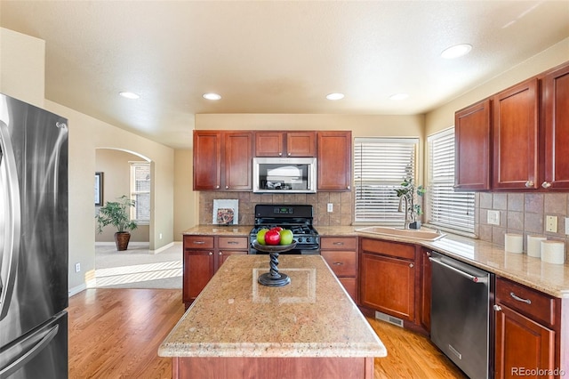 kitchen with light stone countertops, tasteful backsplash, stainless steel appliances, sink, and a center island