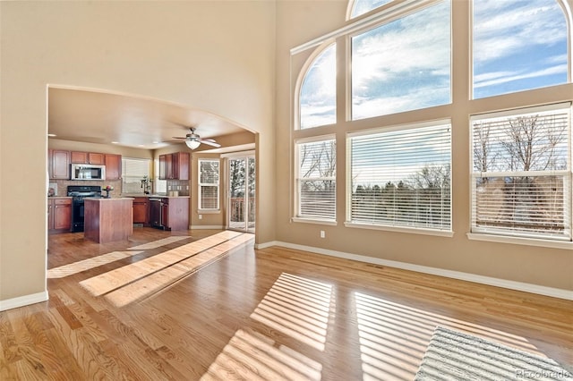 unfurnished living room featuring a towering ceiling, light wood-type flooring, and ceiling fan