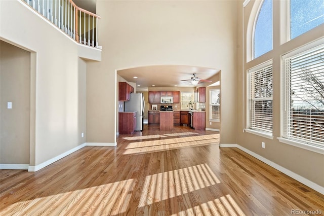 unfurnished living room featuring ceiling fan, light hardwood / wood-style floors, a towering ceiling, and sink