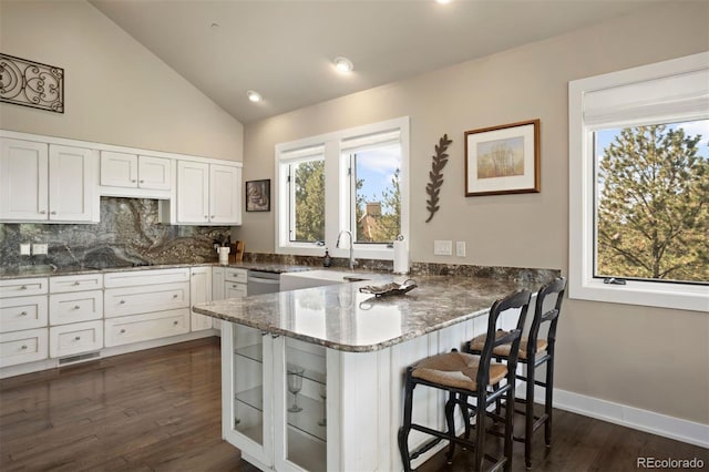 kitchen featuring kitchen peninsula, white cabinetry, a healthy amount of sunlight, and a kitchen bar