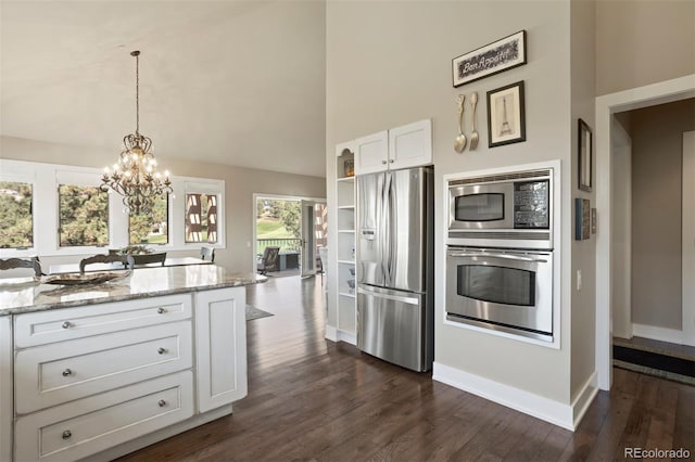 kitchen with white cabinets, appliances with stainless steel finishes, dark hardwood / wood-style floors, a towering ceiling, and light stone counters