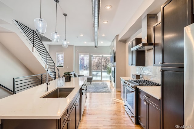 kitchen featuring wall chimney exhaust hood, appliances with stainless steel finishes, a sink, light wood-type flooring, and backsplash