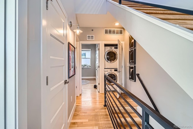 hallway featuring light wood finished floors, visible vents, stacked washer / drying machine, and an upstairs landing