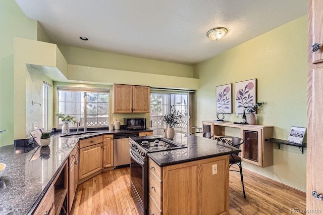 kitchen with light wood-style flooring, dark stone counters, stainless steel appliances, and a sink