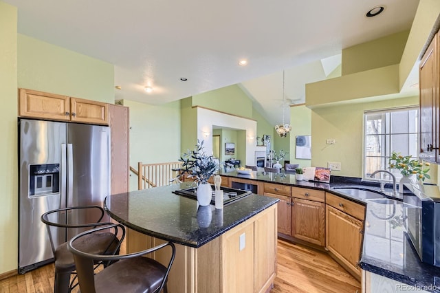 kitchen with light wood-style flooring, gas stovetop, vaulted ceiling, stainless steel fridge with ice dispenser, and a kitchen bar