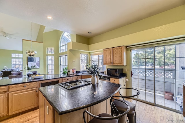 kitchen with black microwave, a breakfast bar area, a center island, light wood finished floors, and cooktop