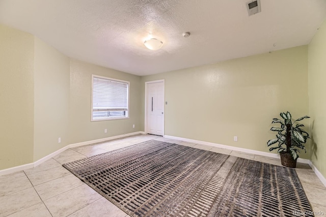 unfurnished room with light tile patterned floors, baseboards, visible vents, and a textured ceiling