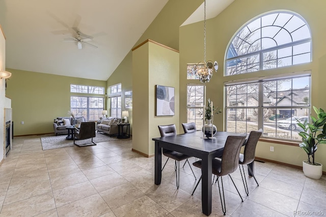 dining space featuring a glass covered fireplace, light tile patterned flooring, baseboards, and ceiling fan with notable chandelier