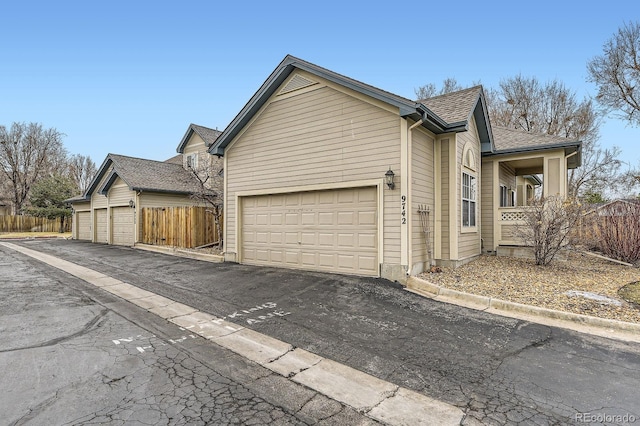 view of side of property featuring a garage, a shingled roof, and fence