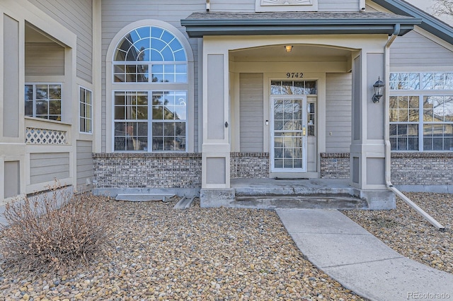 view of exterior entry featuring brick siding and roof with shingles