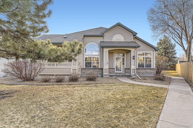 view of front of house featuring brick siding, roof with shingles, a front yard, and fence