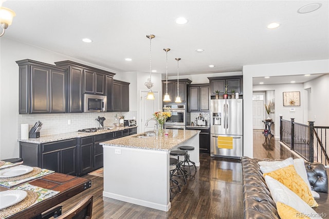 kitchen with dark hardwood / wood-style floors, decorative light fixtures, a center island with sink, a breakfast bar, and stainless steel appliances