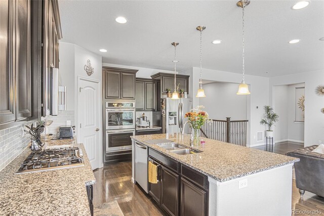 kitchen featuring a center island with sink, dark wood-type flooring, stainless steel appliances, sink, and light stone counters