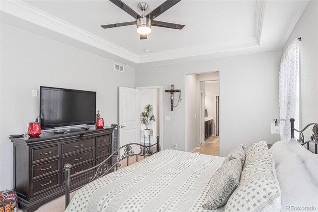 bedroom with a tray ceiling, ceiling fan, connected bathroom, and ornamental molding