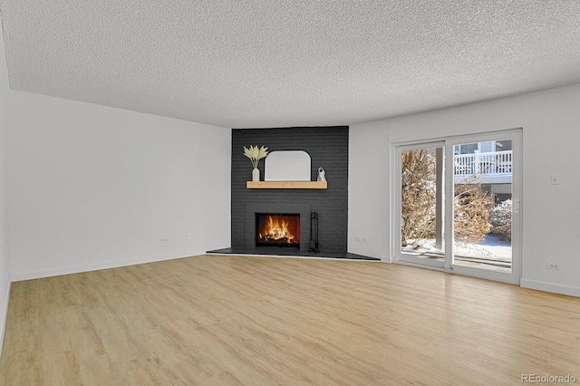 unfurnished living room with a brick fireplace, a textured ceiling, and light hardwood / wood-style floors