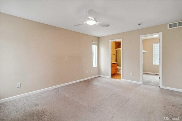 unfurnished bedroom featuring light colored carpet, baseboards, connected bathroom, and a ceiling fan