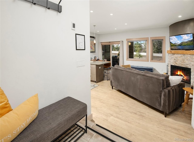 living area featuring recessed lighting, a stone fireplace, and light wood-style flooring