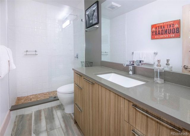 full bath with vanity, toilet, tiled shower, and visible vents