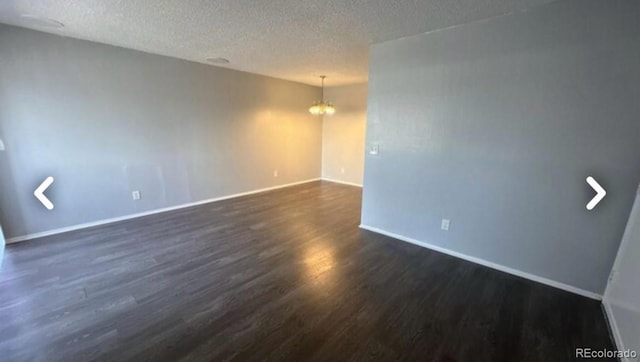 unfurnished room with dark wood-style flooring, a notable chandelier, a textured ceiling, and baseboards