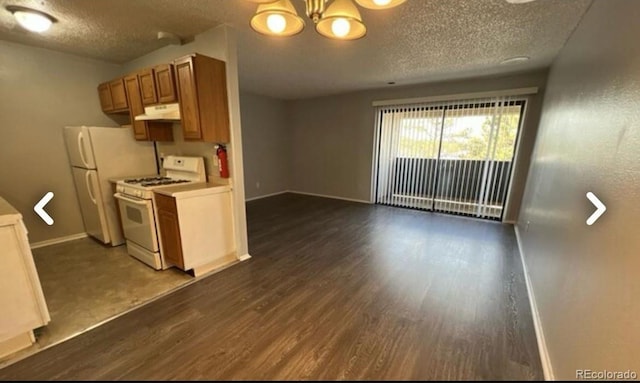 kitchen featuring white appliances, dark wood finished floors, under cabinet range hood, and baseboards