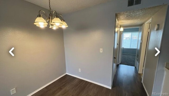 unfurnished room with a textured ceiling, visible vents, baseboards, dark wood-style floors, and an inviting chandelier