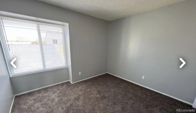 spare room with a textured ceiling, dark carpet, and baseboards