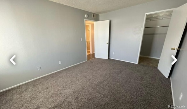 unfurnished bedroom with a walk in closet, dark colored carpet, a closet, visible vents, and a textured ceiling