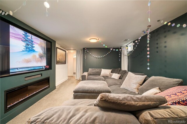 home theater featuring visible vents, baseboards, a glass covered fireplace, and light carpet
