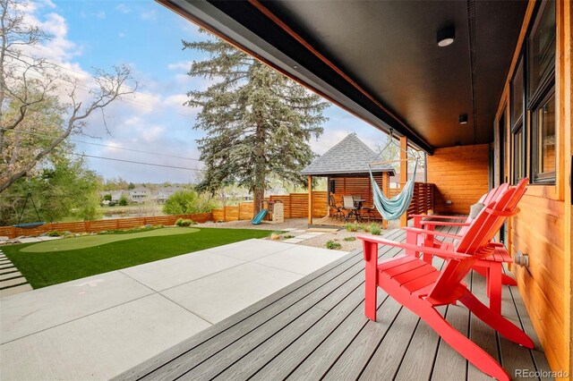 deck with a playground, a lawn, a fenced backyard, and a patio area