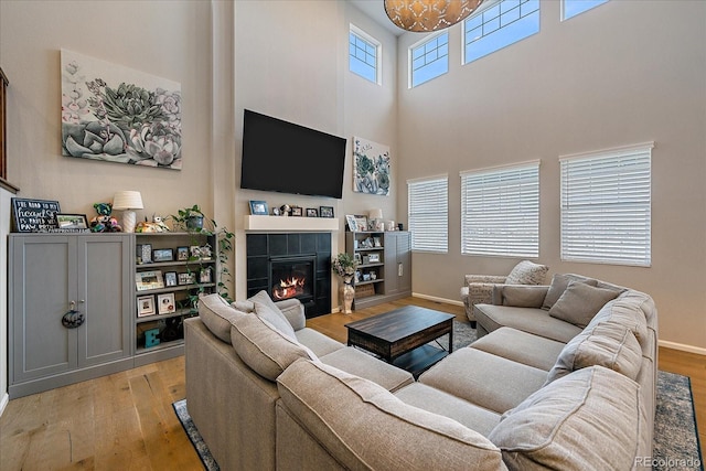 living area with a high ceiling, baseboards, light wood finished floors, and a tile fireplace