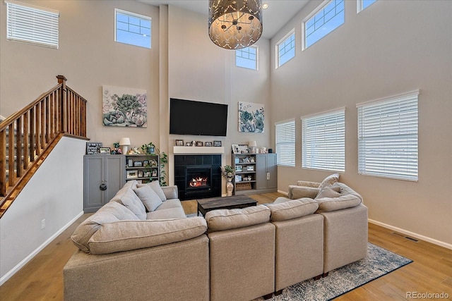 living room featuring visible vents, a tiled fireplace, stairway, light wood finished floors, and baseboards