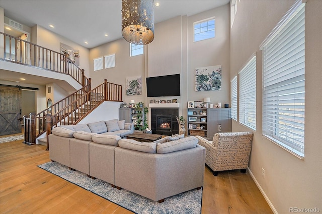 living area with stairway, wood finished floors, baseboards, a glass covered fireplace, and a barn door